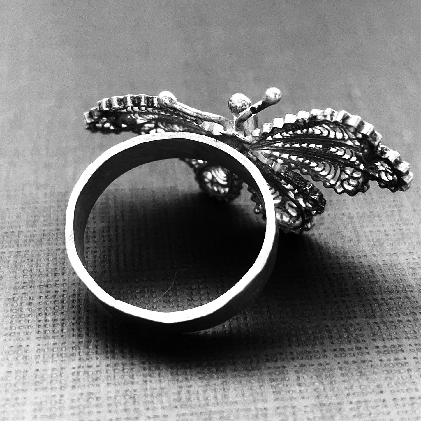 The bsck view showing a solid silver band ring topped with antique butterfly made of hundreds of coiled silver strands. 